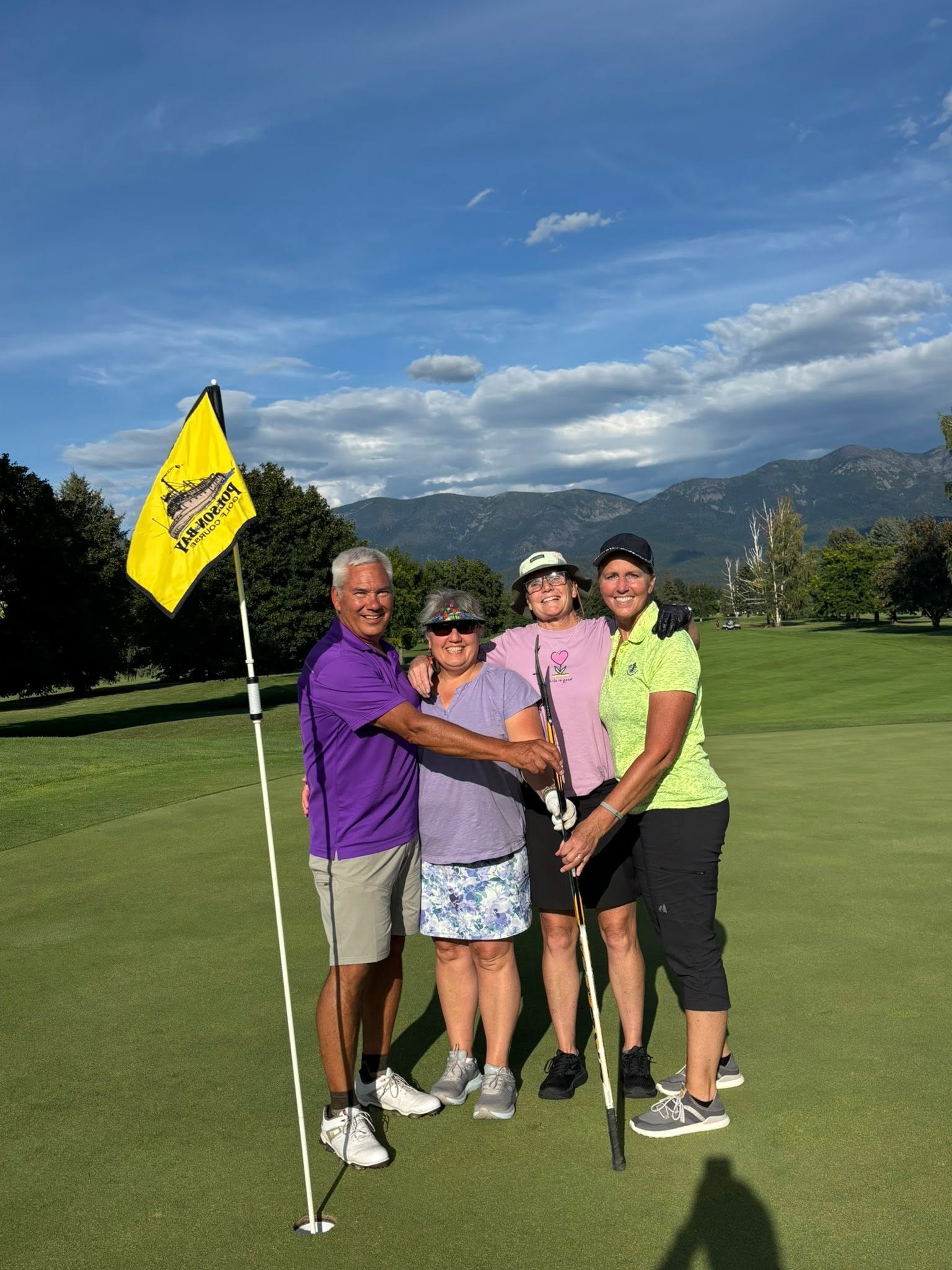 Four tournament participants standing together on a putting green beside a yellow course flag.