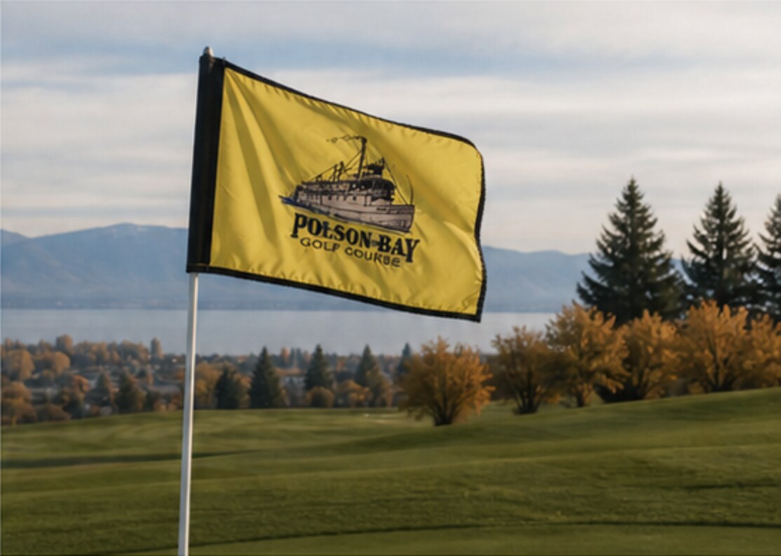 A yellow Polson Bay Golf Course flag overlooking the course, Flathead Lake, and the Mission Mountains.