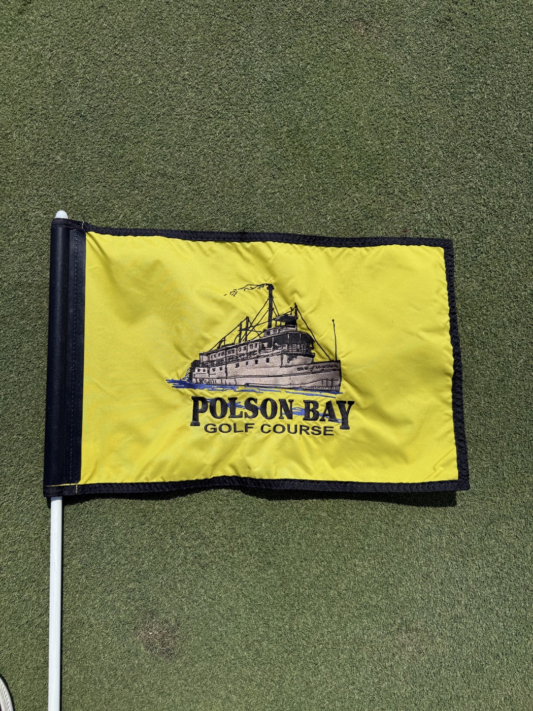Yellow Polson Bay Golf Course flag resting on the putting green.